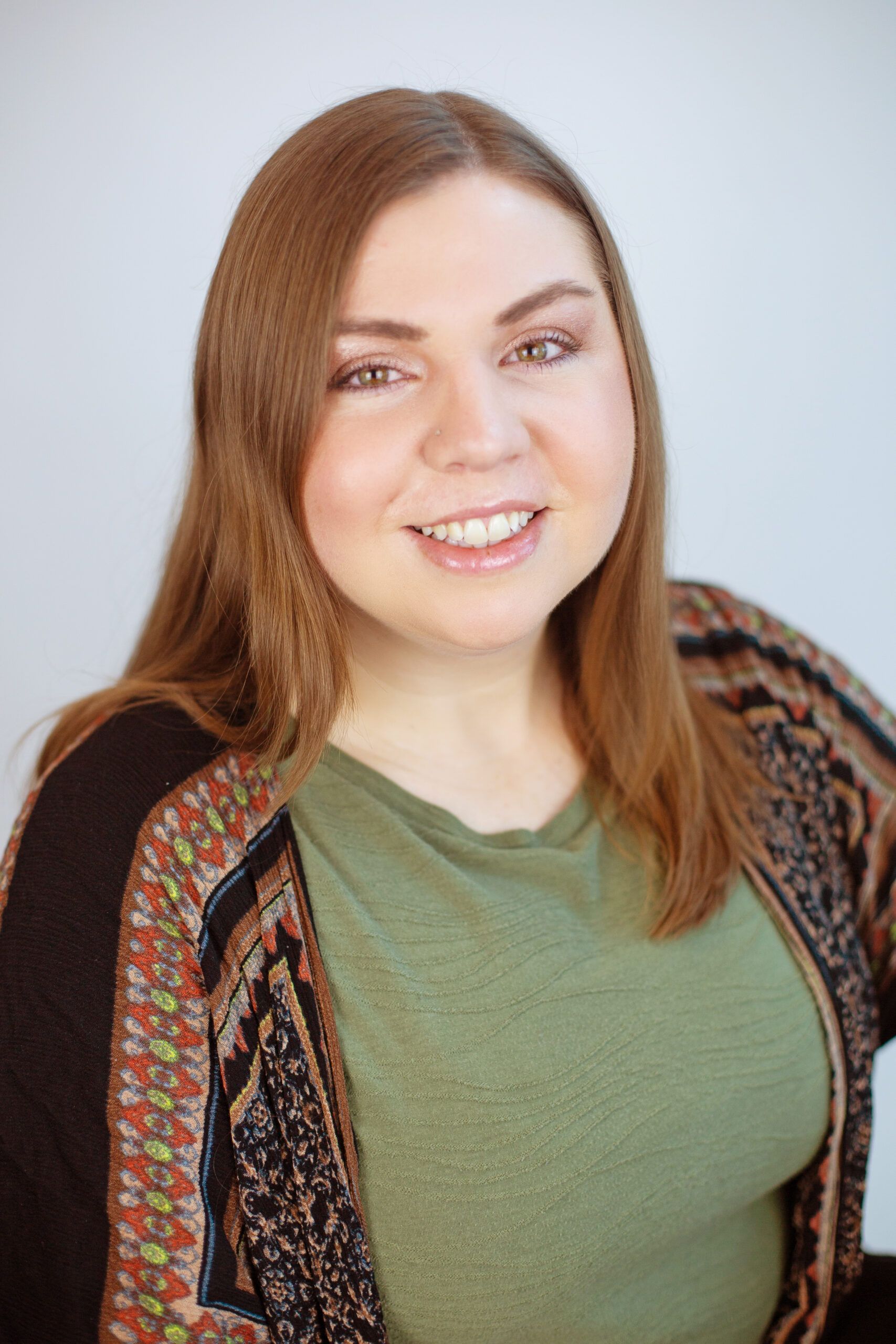 A woman wearing a green shirt and a cardigan is smiling for the camera.