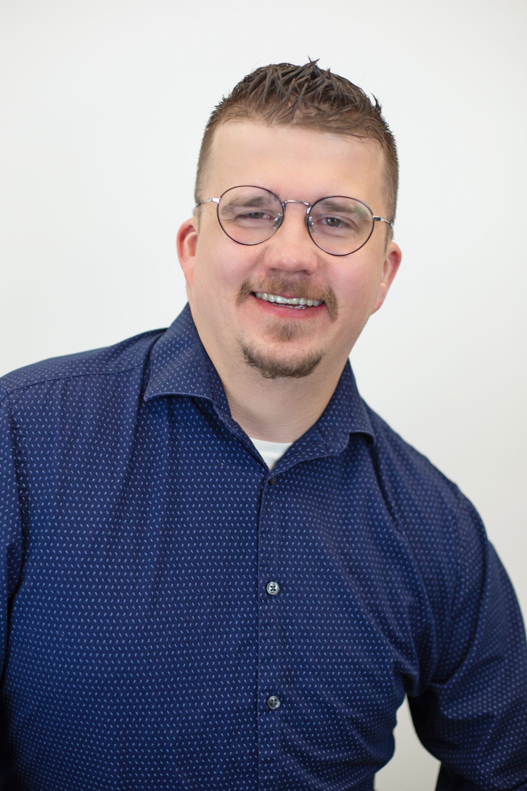 A man wearing glasses and a blue shirt is smiling for the camera.