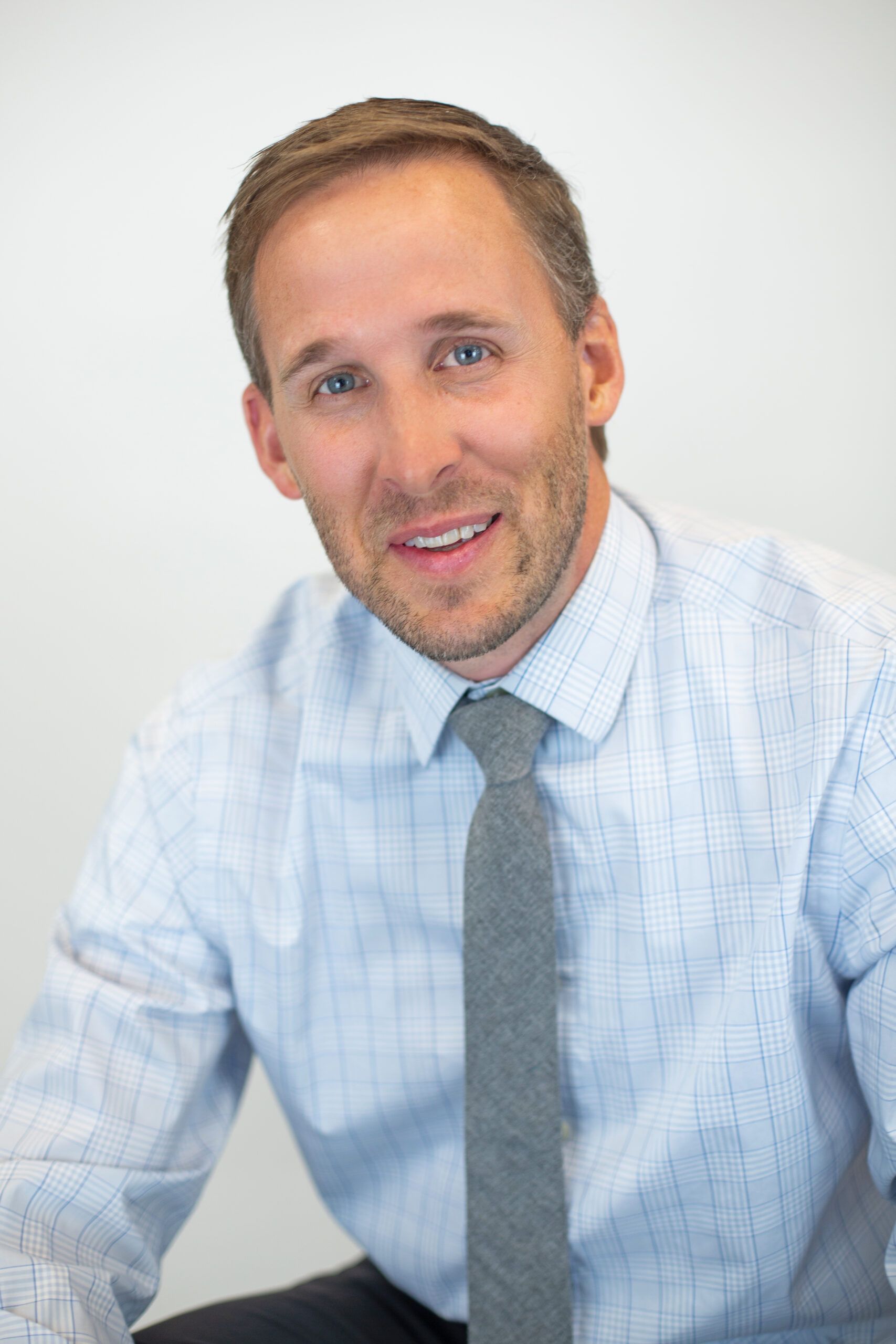 A man in a blue shirt and tie is smiling for the camera.