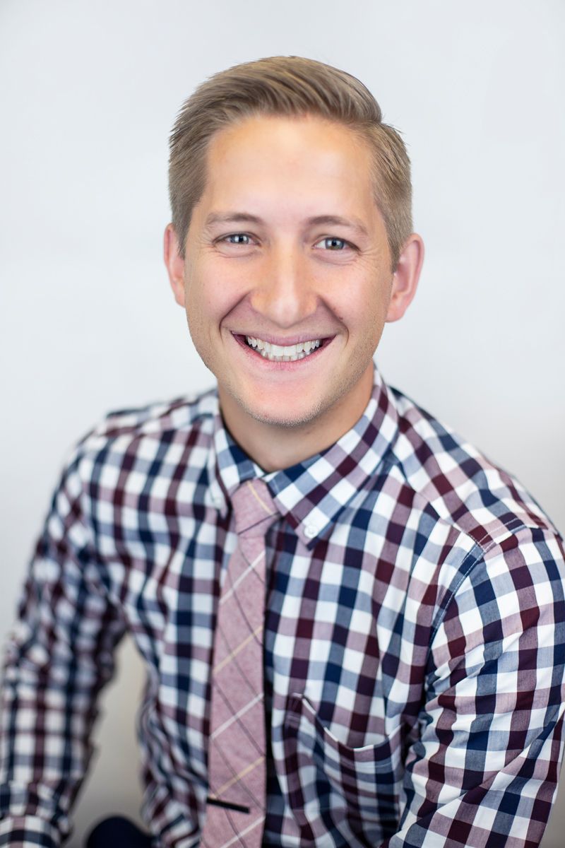 A man in a plaid shirt and tie is smiling for the camera.