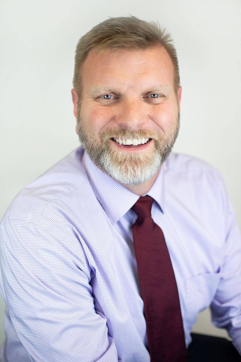 A man with a beard is wearing a purple shirt and red tie.