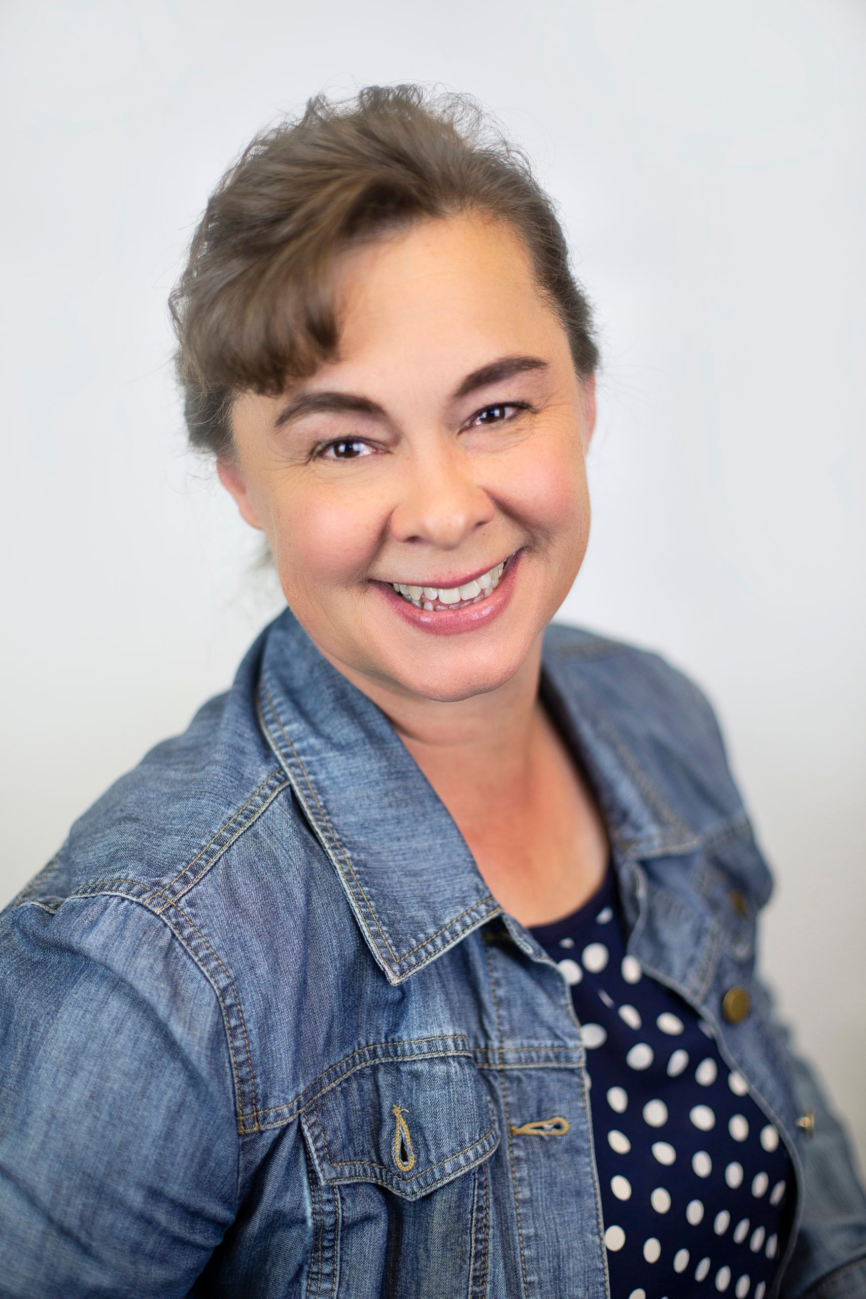 A woman wearing a denim jacket and polka dot shirt is smiling for the camera.