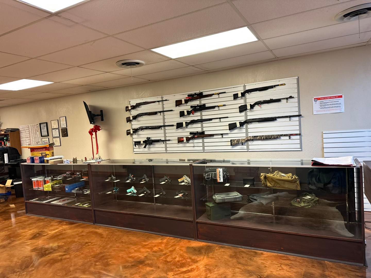 Firearms displayed in a store behind glass counters. Rifles mounted on white wall panels.