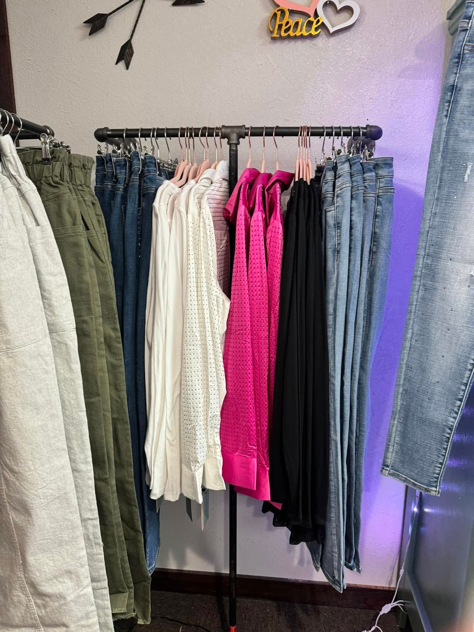 Clothing rack with various colored garments hanging; jeans, tops, and pants.
