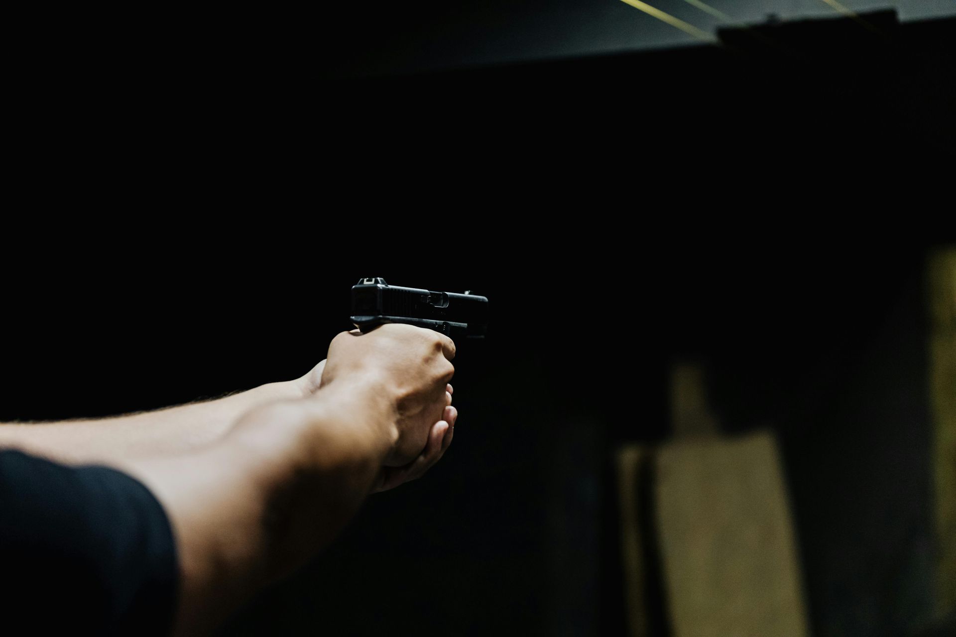 Person holding a handgun, aiming at a target in a dark shooting range.