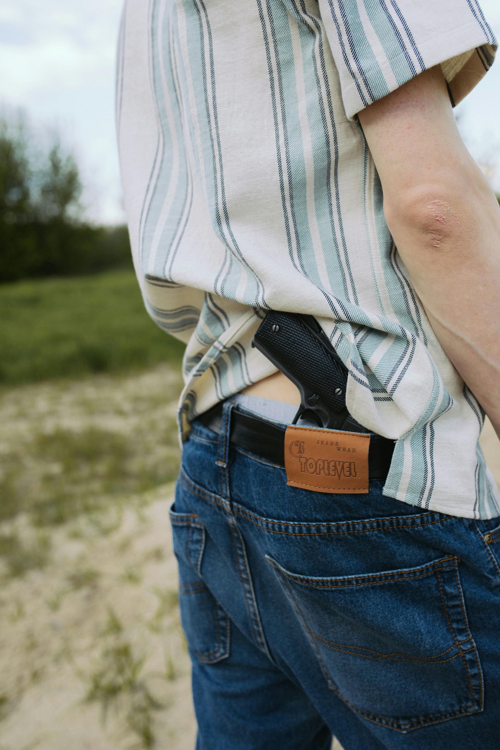 Person with a handgun in a holster on their back, visible behind their jeans and shirt.