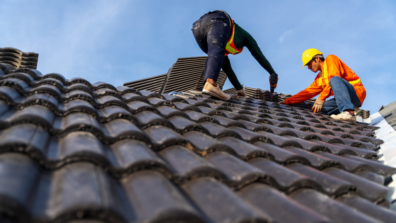 Two roofers installing dark grey ceramic tiles on a rooftop.