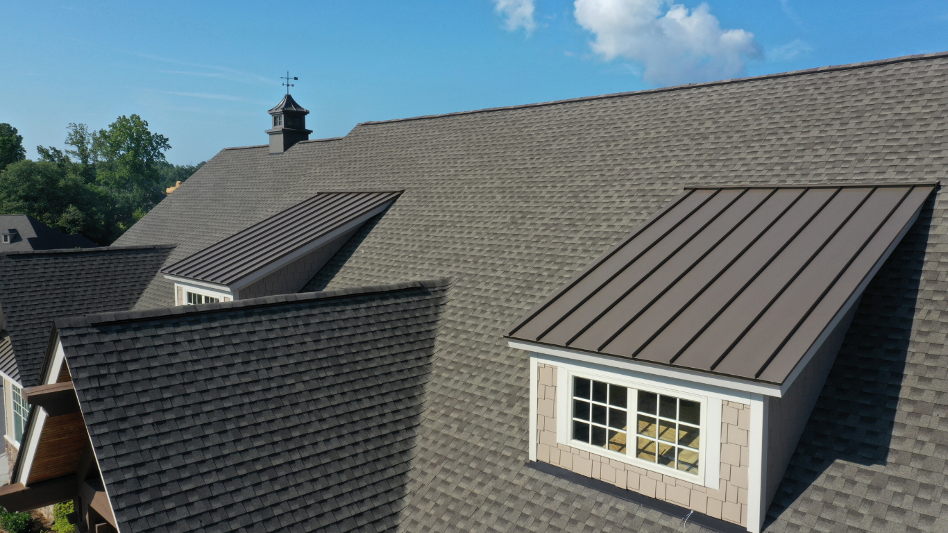 Brown shingled roof with metal dormers and cupola against a partly cloudy sky.