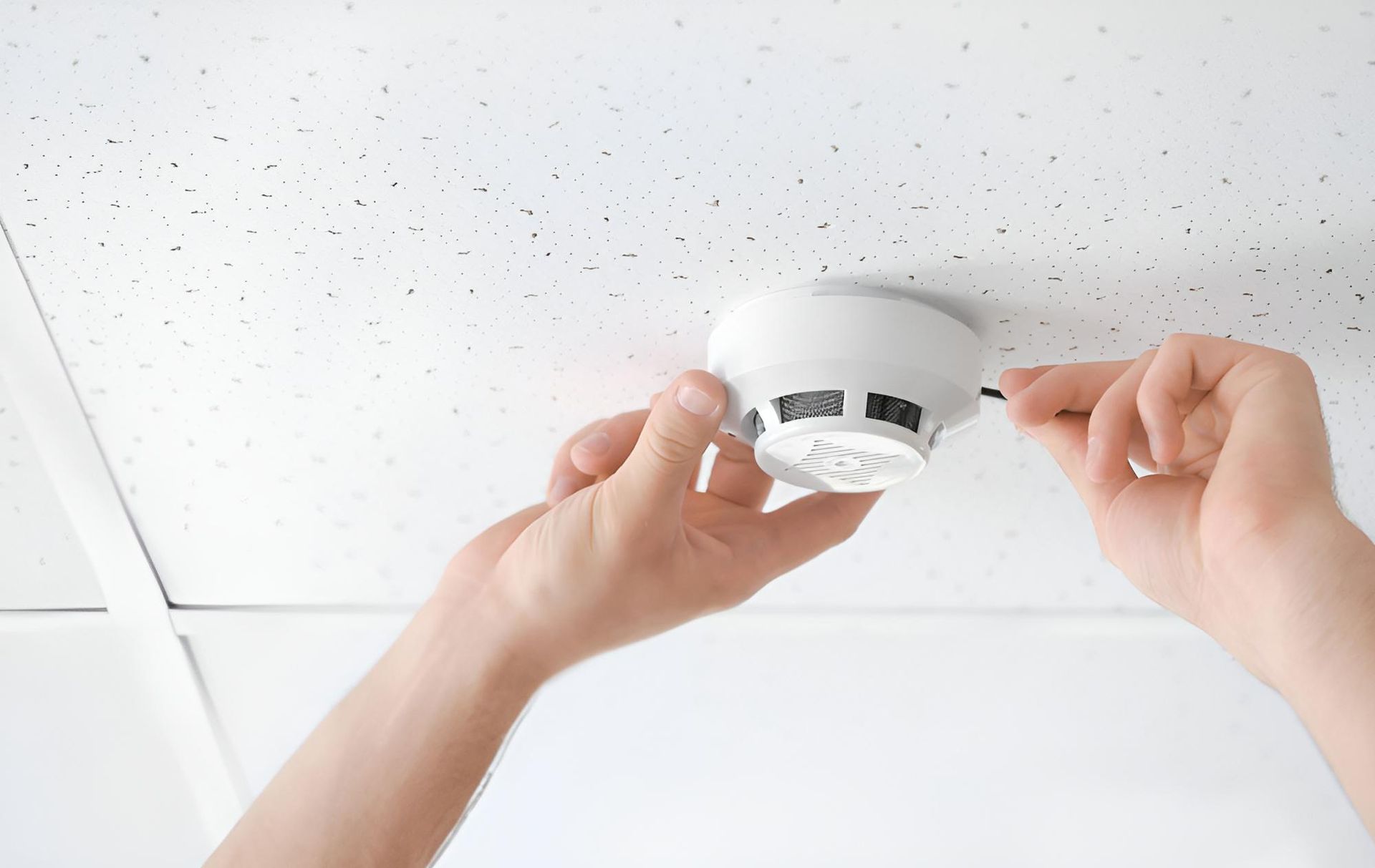A Person is Installing a Smoke Detector on the Ceiling — Reilly Electrical Services in Maroochydore, QLD