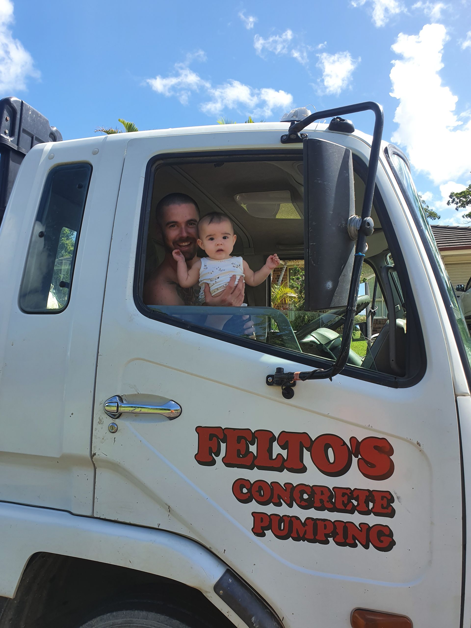 Man holding baby inside a concrete pumping truck with Felto’s logo— Felto's Concrete Line Pumping in Coffs Harbour, NSW