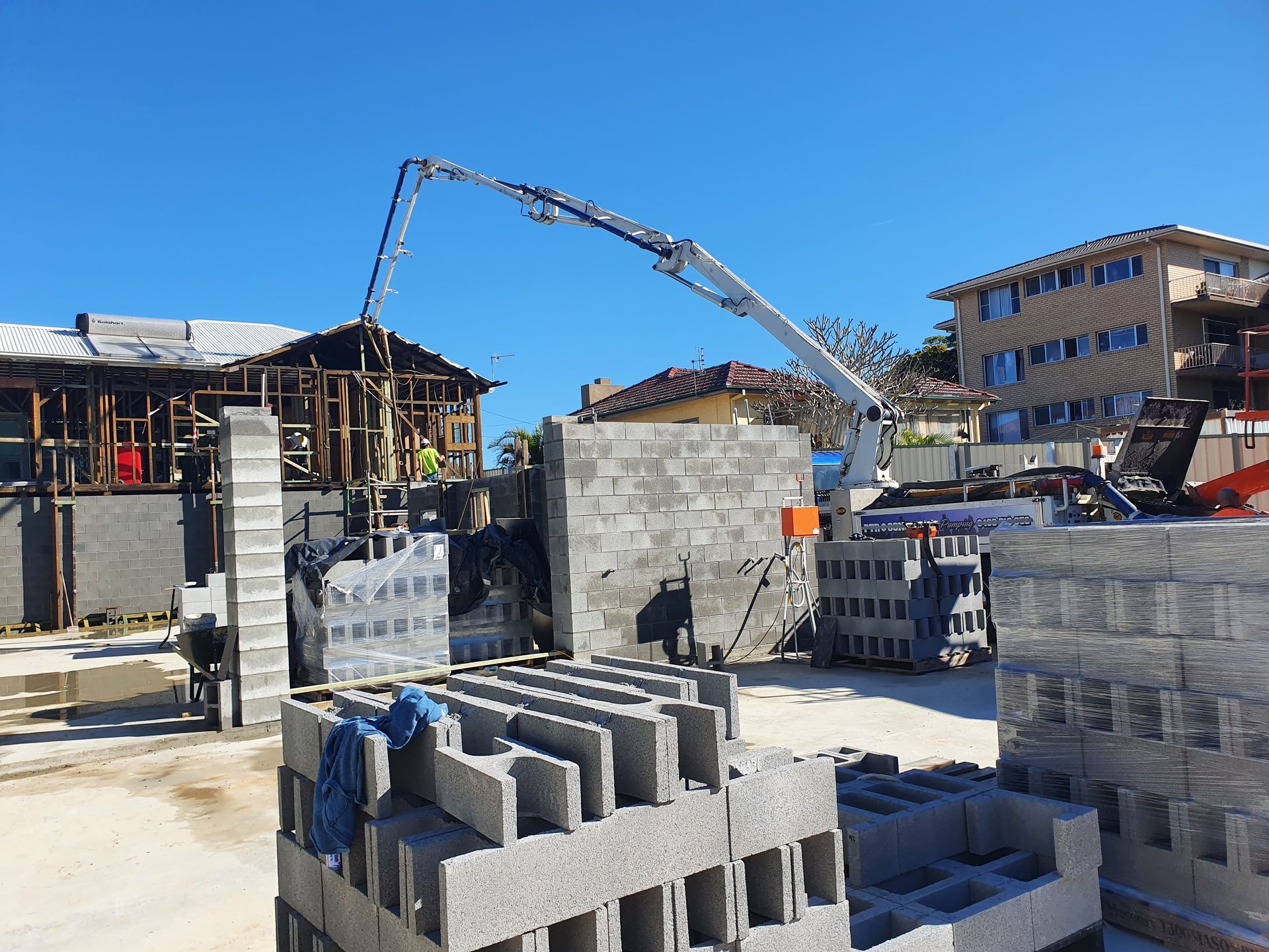 Construction site with a concrete pump pouring concrete into a building. Grey blocks are stacked nearby.