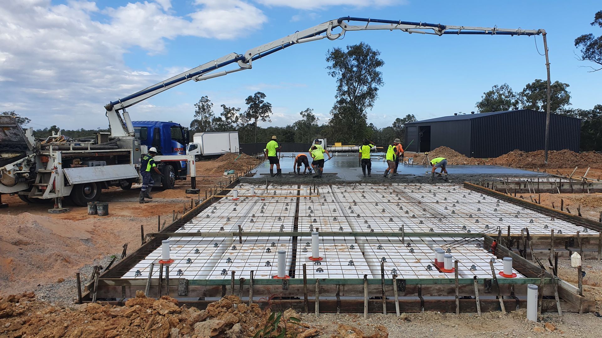Concrete being poured onto a prepared foundation at a construction site with a concrete pump truck and workers.