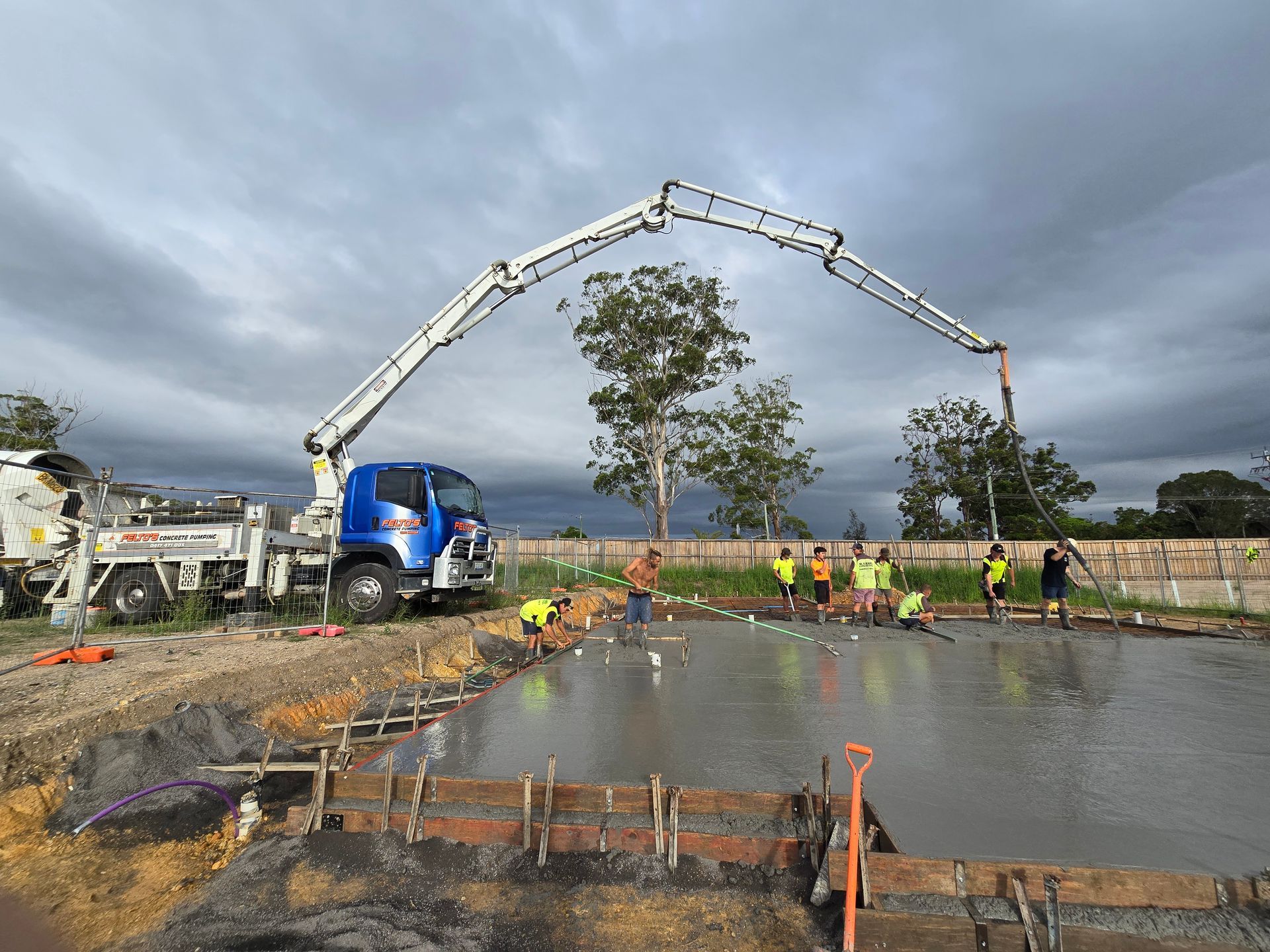 Felto’s boom pump placing concrete slab with workers smoothing surface — Felto's Concrete Line Pumping in Coffs Harbour, NSW.