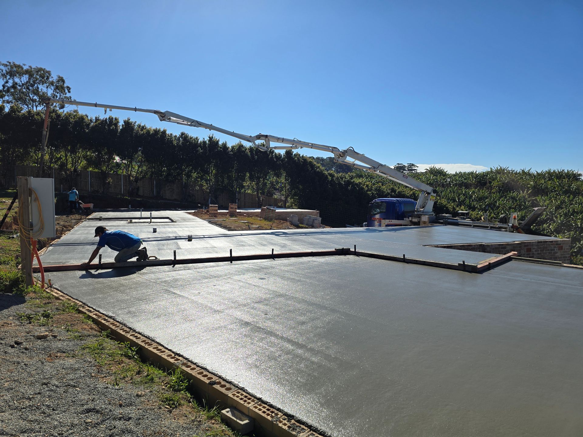 Worker finishing a large concrete slab with Felto’s boom pump in background — Felto's Concrete Line Pumping in Coffs Harbour, NSW.