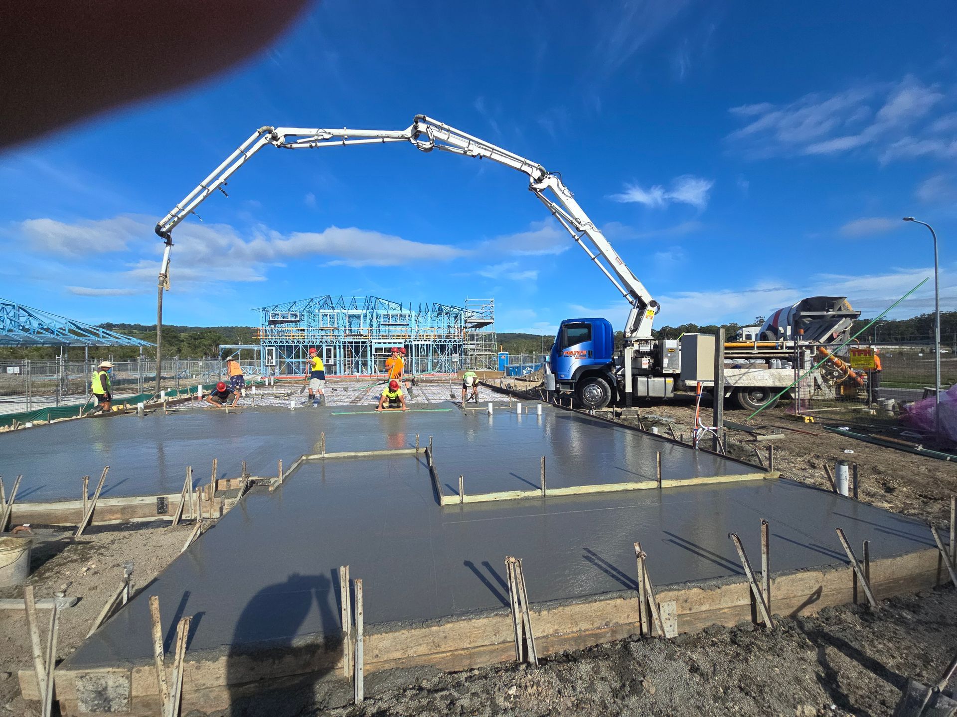 Construction site with concrete being poured by a pump truck. Workers in safety vests. Bright blue sky.