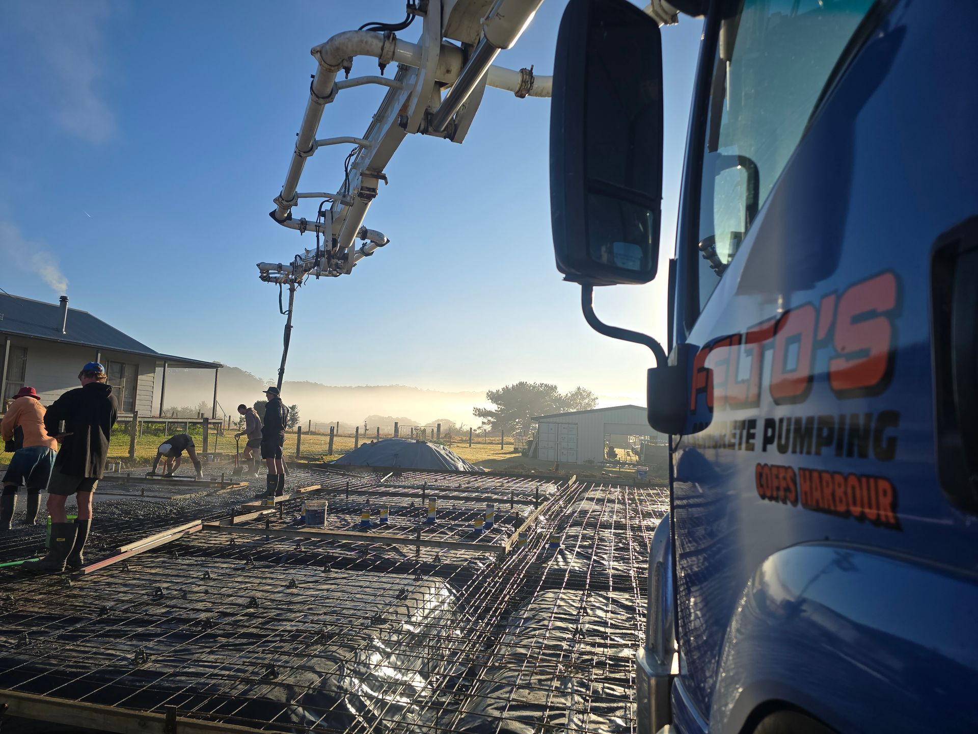 Felto’s boom pump truck pouring concrete slab in early morning light — Felto's Concrete Line Pumping in Coffs Harbour, NSW.