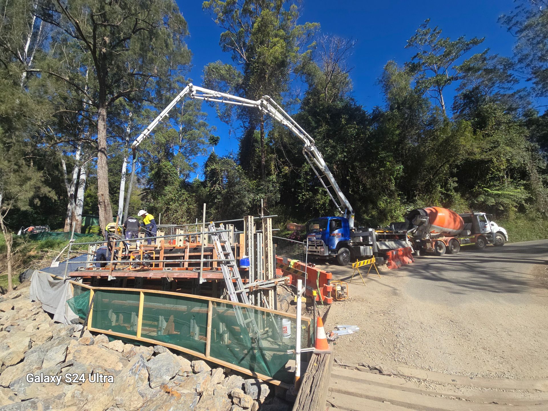 Construction site: concrete pump truck pouring concrete into a bridge form. Workers are present.