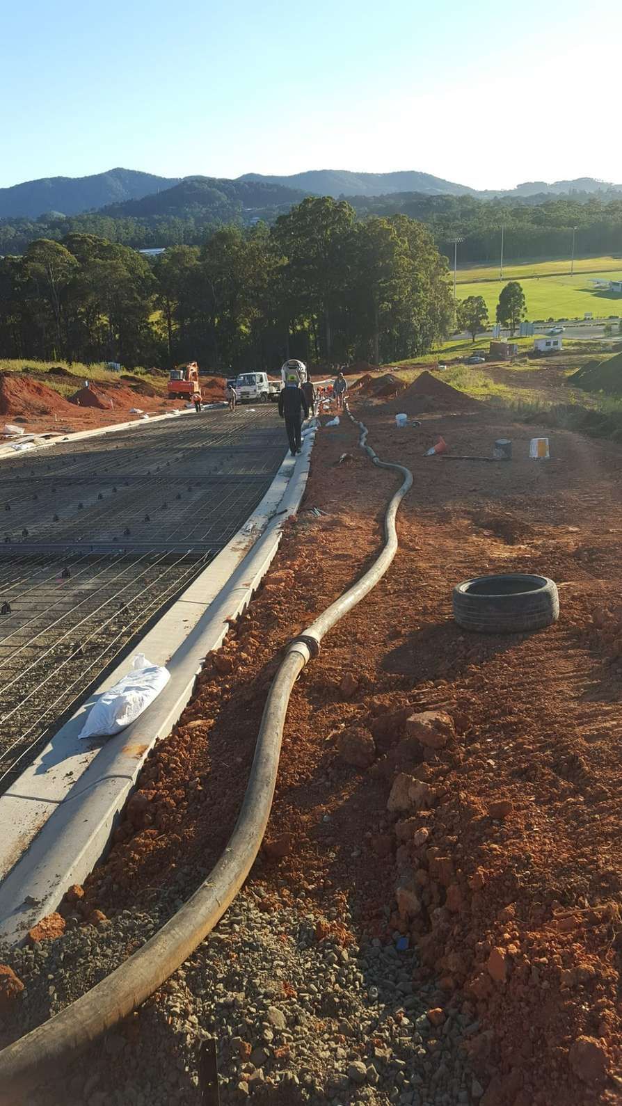 A Man is Walking Down a Dirt Road Next to a Hose — Felto's Concrete Line Pumping in Woolgoolga, NSW