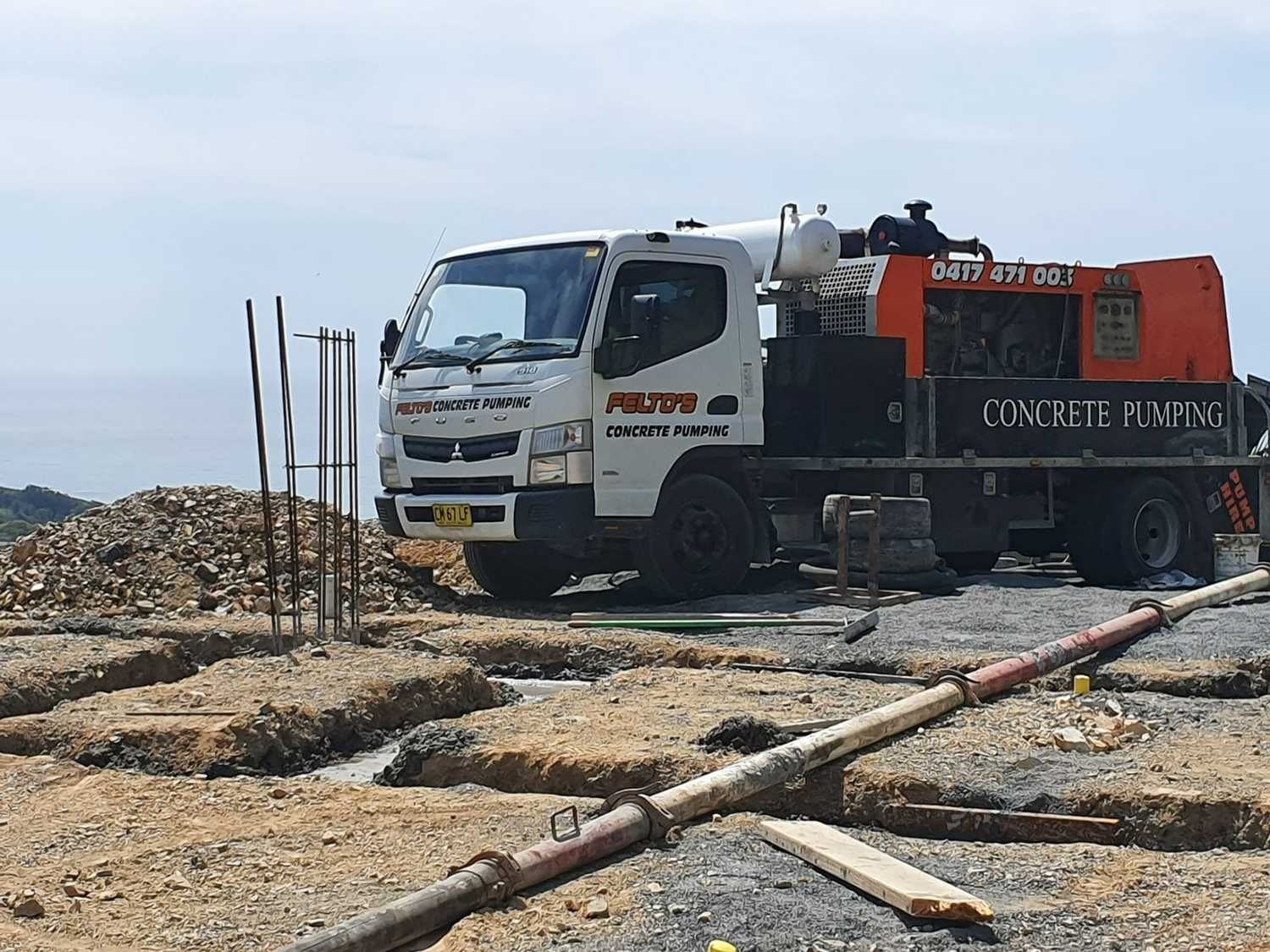 A Truck With a Pump Attached to It is Parked in a Dirt Field — Felto's Concrete Line Pumping in Sawtell, NSW