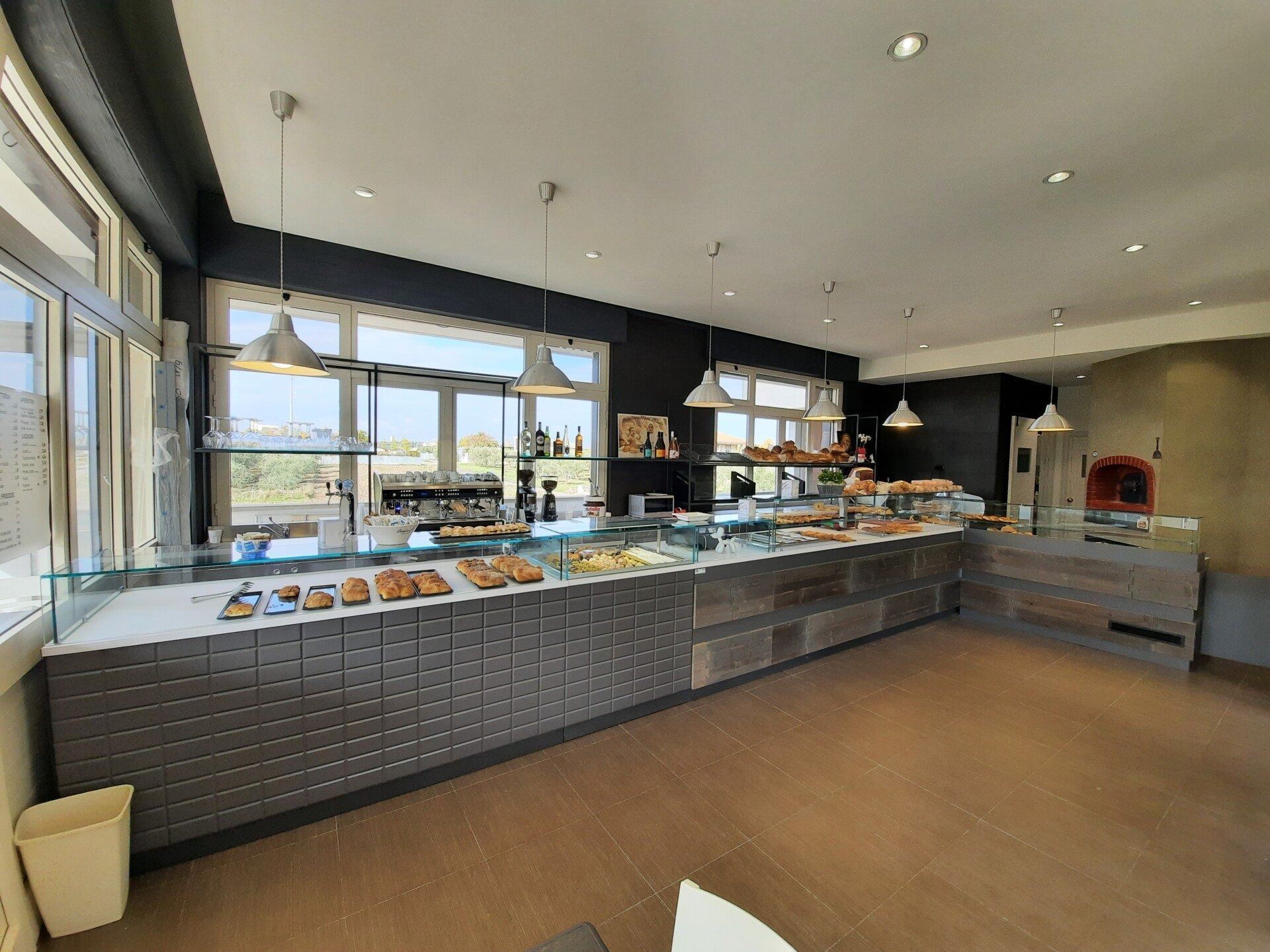 Luminoso bancone buffet in una sala da pranzo moderna con ampie finestre e lampade a sospensione.