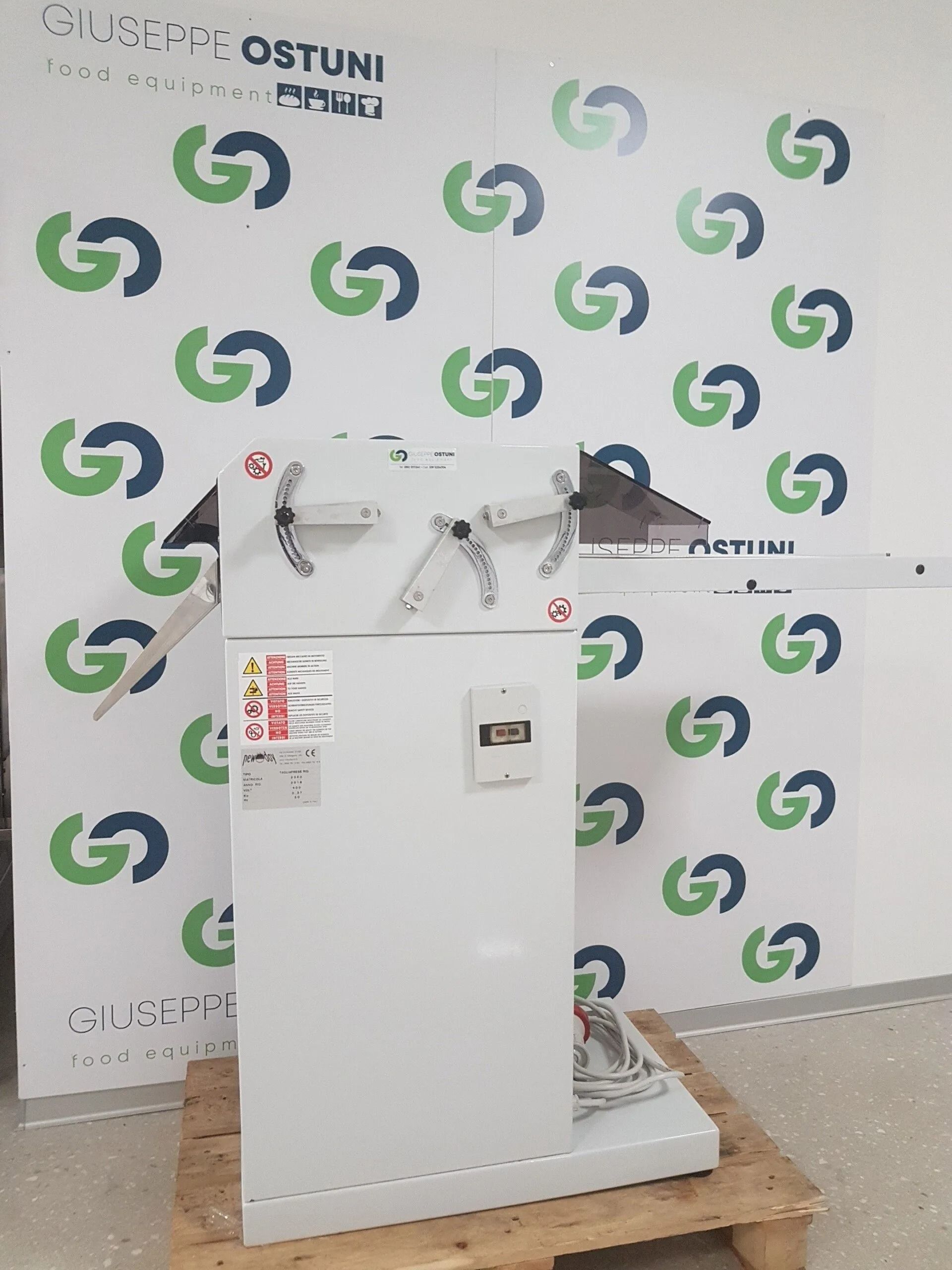 Macchinario industriale bianco su un pallet di legno, appoggiato a una parete con il marchio Ostuni Energy.