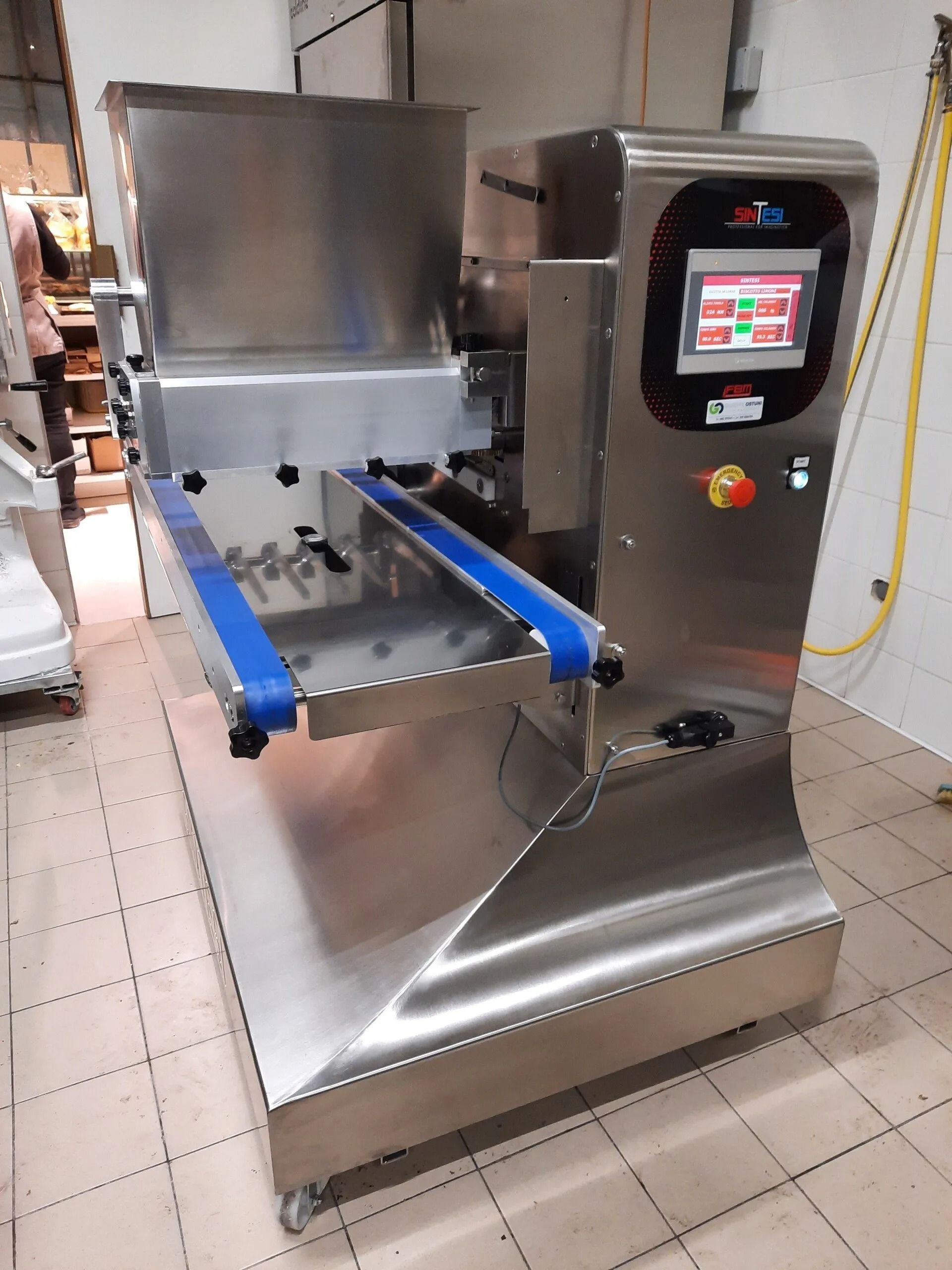 Macchina industriale in acciaio inox con binari blu e pannello di controllo touchscreen in un'officina