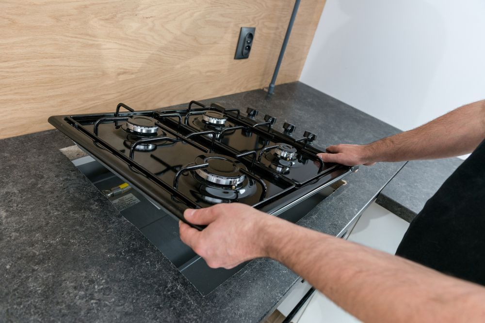 Person Installing a Black Gas Cooktop in a Kitchen Countertop — David McNeill Plumma (Gas Specialist) In Cessnock, NSW