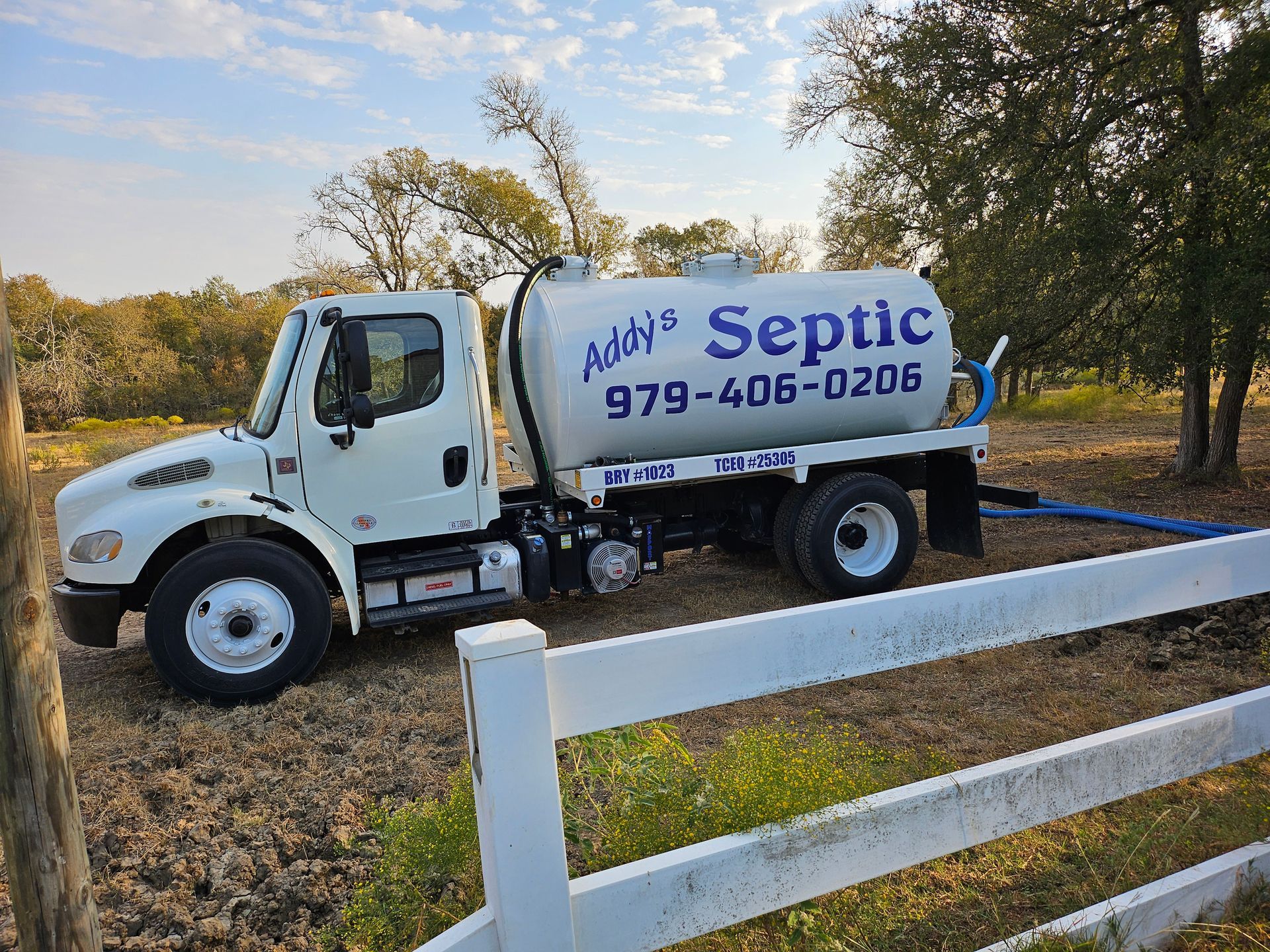 A white septic truck is parked next to a white fence