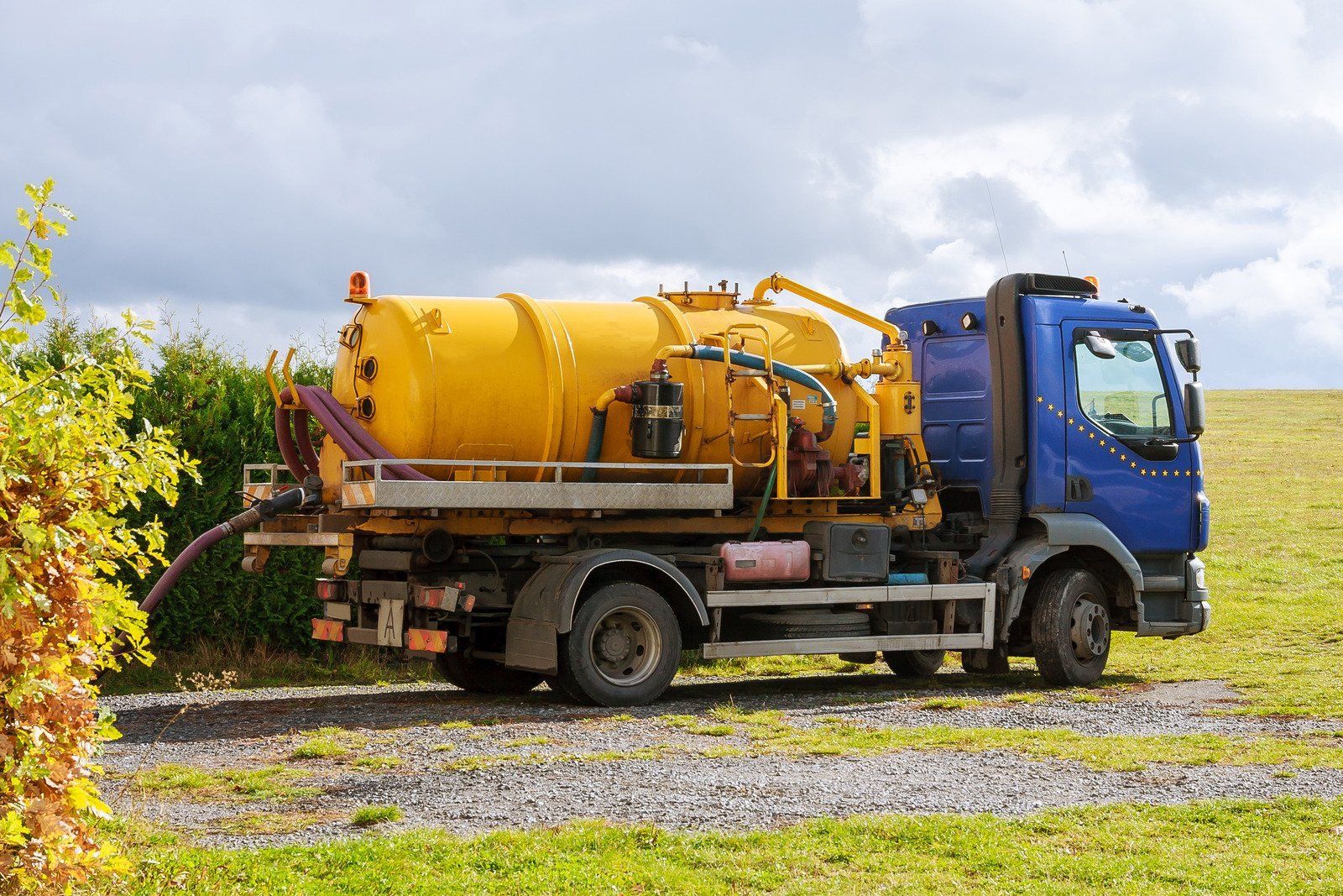 A yellow and blue vacuum truck is parked in a grassy field.