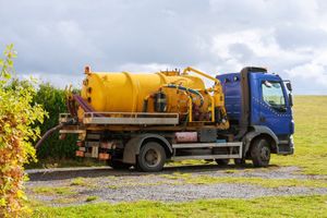 A yellow and blue vacuum truck is parked in a grassy field.