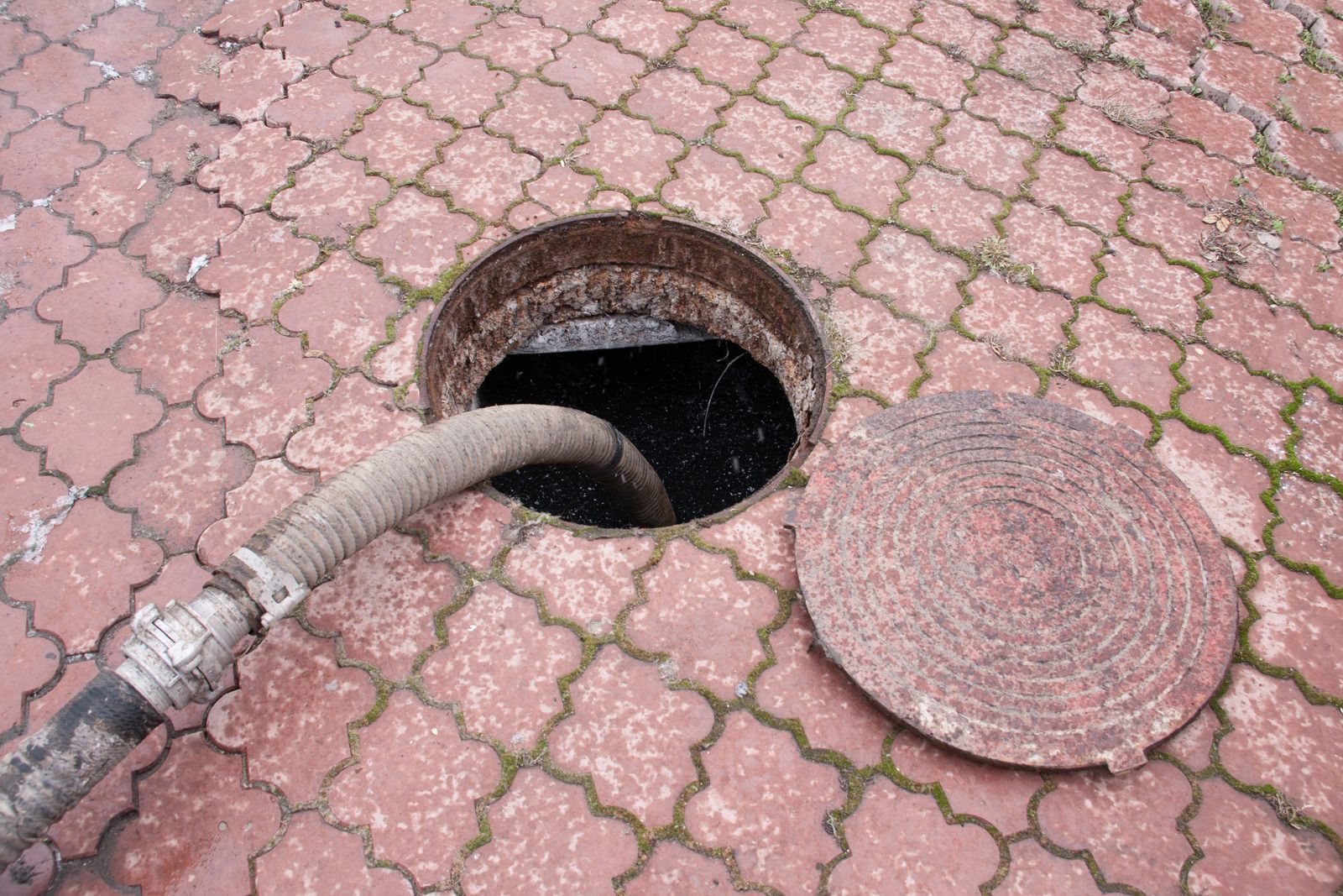 A manhole cover is open and a hose is coming out of it.