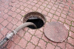 A manhole cover is open and a hose is coming out of it.