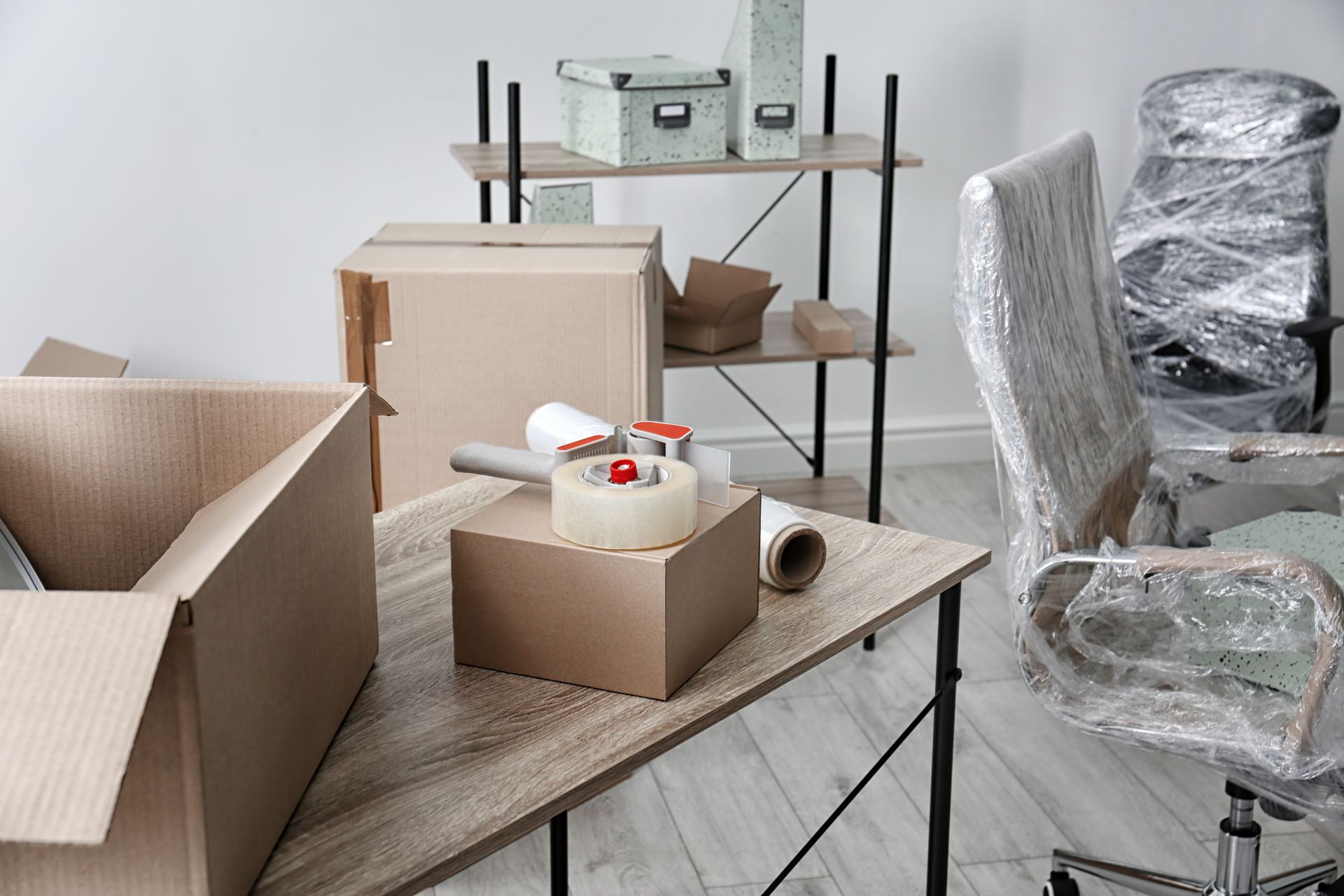 a room filled with boxes , tape , and a chair wrapped in plastic .