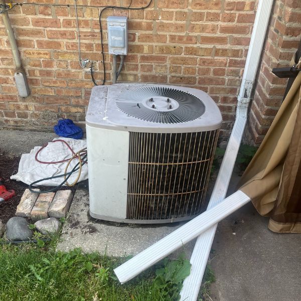 An air conditioning unit against a brick wall with exposed wires and tubing.