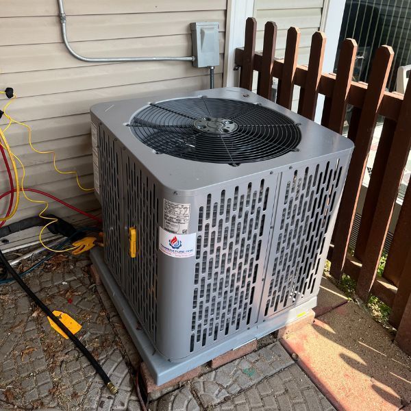 Gray air conditioning unit on a brick base next to a fence.