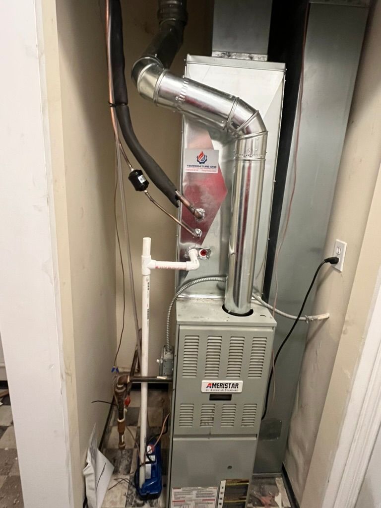 Furnace in a utility closet with silver exhaust pipe and various pipes and wires.
