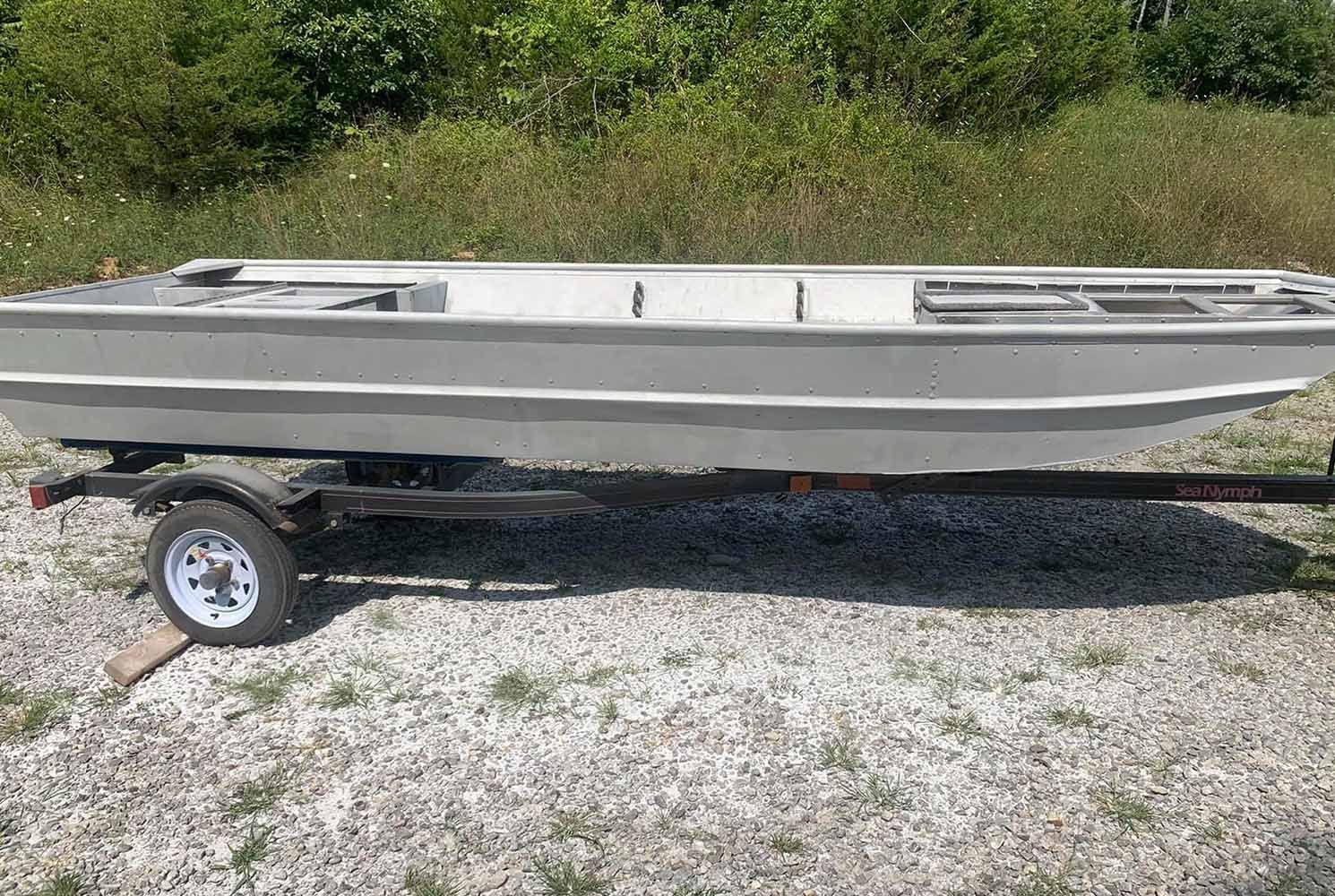 A boat is sitting on a trailer on a gravel road.