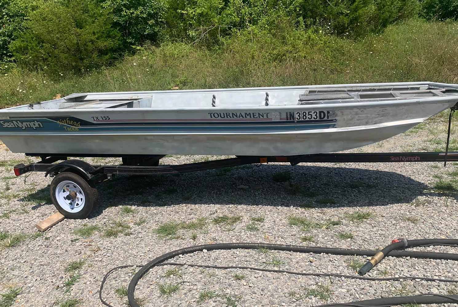 A small boat is sitting on a trailer on a gravel road.