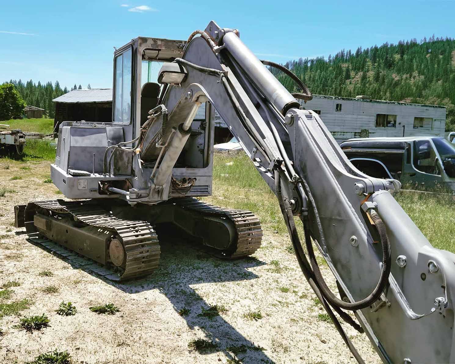 A white excavator is parked in a dirt field