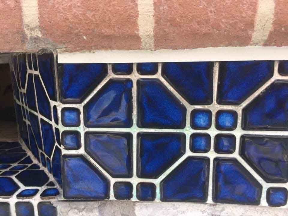 A close up of a blue tile on a brick wall.