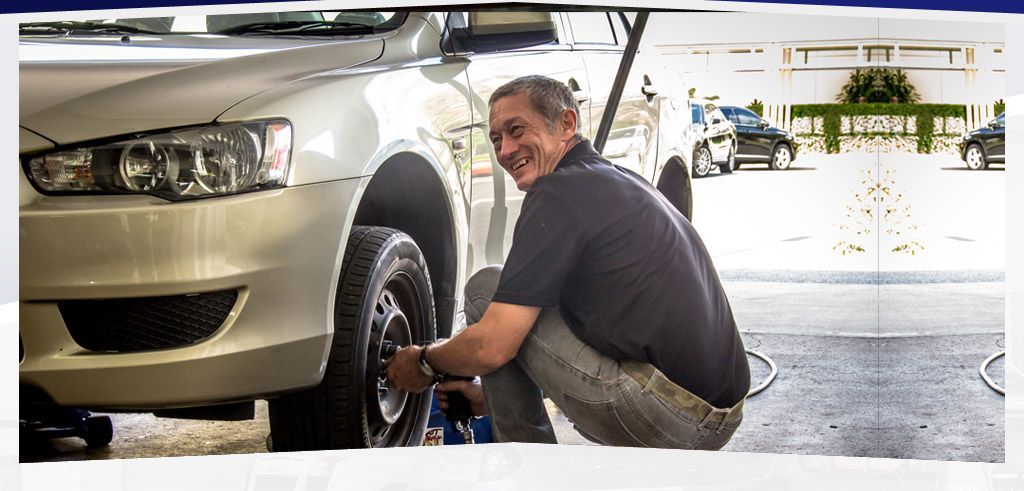 Man Squats Near a White Car, Tightening a Tire — Cairns Tyre Specialists In Cairns City, QLD