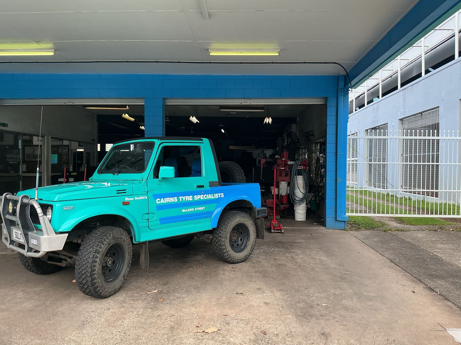 Turquoise Jeep Parked in Front of a Blue Auto Shop — Cairns Tyre Specialists In Cairns City, QLD