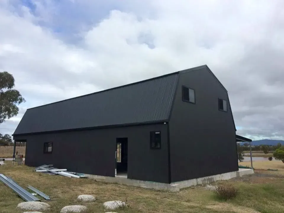 Black barn-style building with a corrugated metal roof. Two small windows on the side and a door opening.