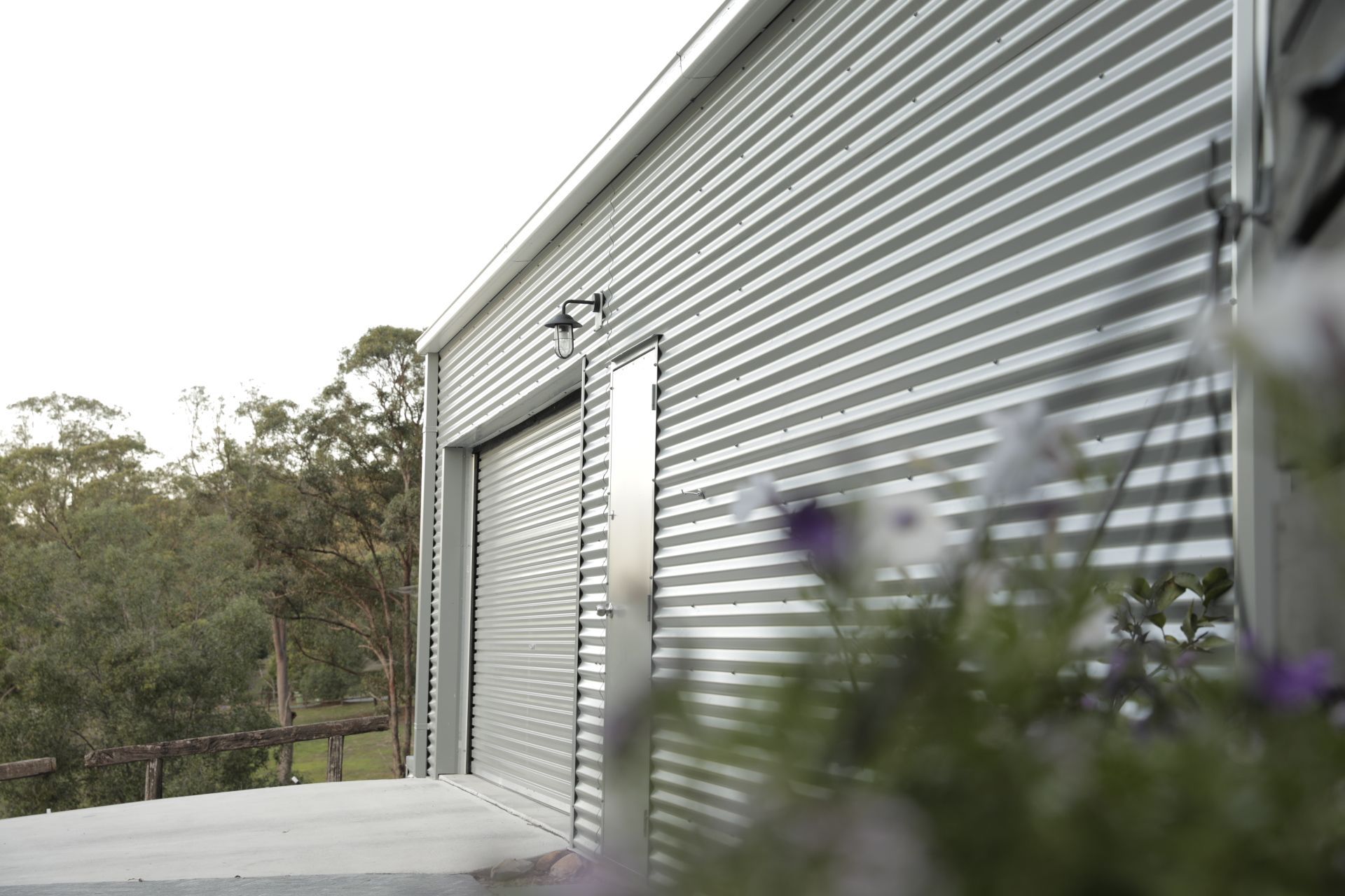 Corrugated metal building with garage door and side door, trees in background, gray and white.
