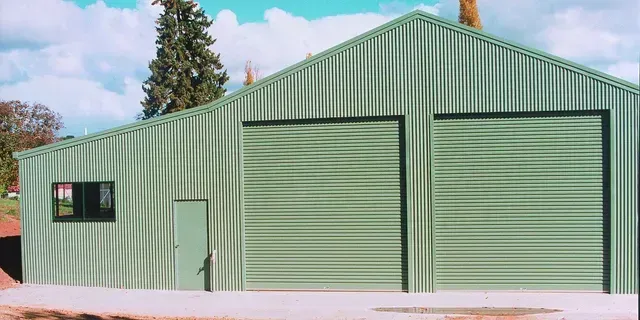 Green corrugated metal building with two garage doors and a small window.