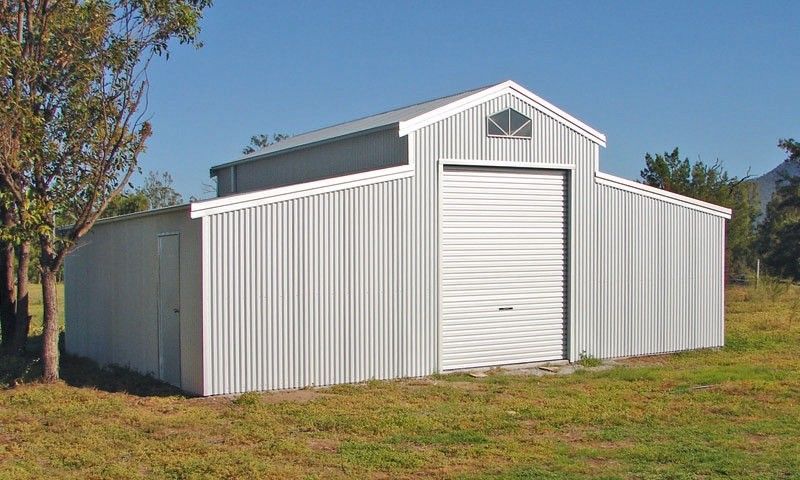 Metal barn with a roll-up door, white siding, and a small attic window. Set on a grassy area.