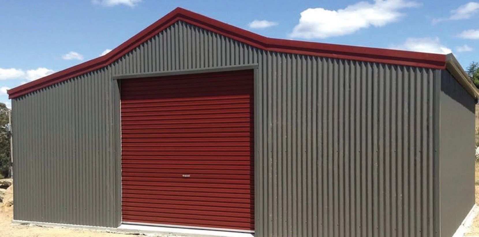 A metal shed with a red garage door and trim against a blue sky.