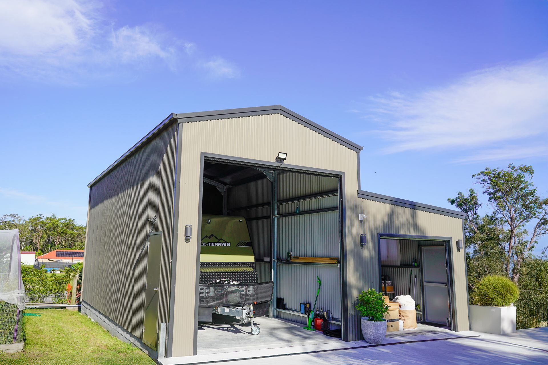 Metal garage with open bay for vehicle, adjacent door. Light blue sky background.