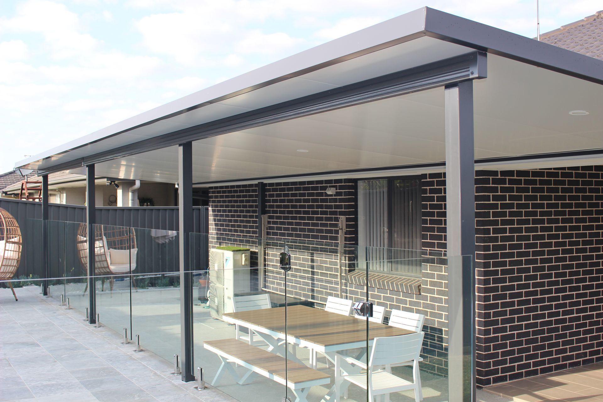 Patio with glass railing, brick wall, dining table, and dark gray roof.