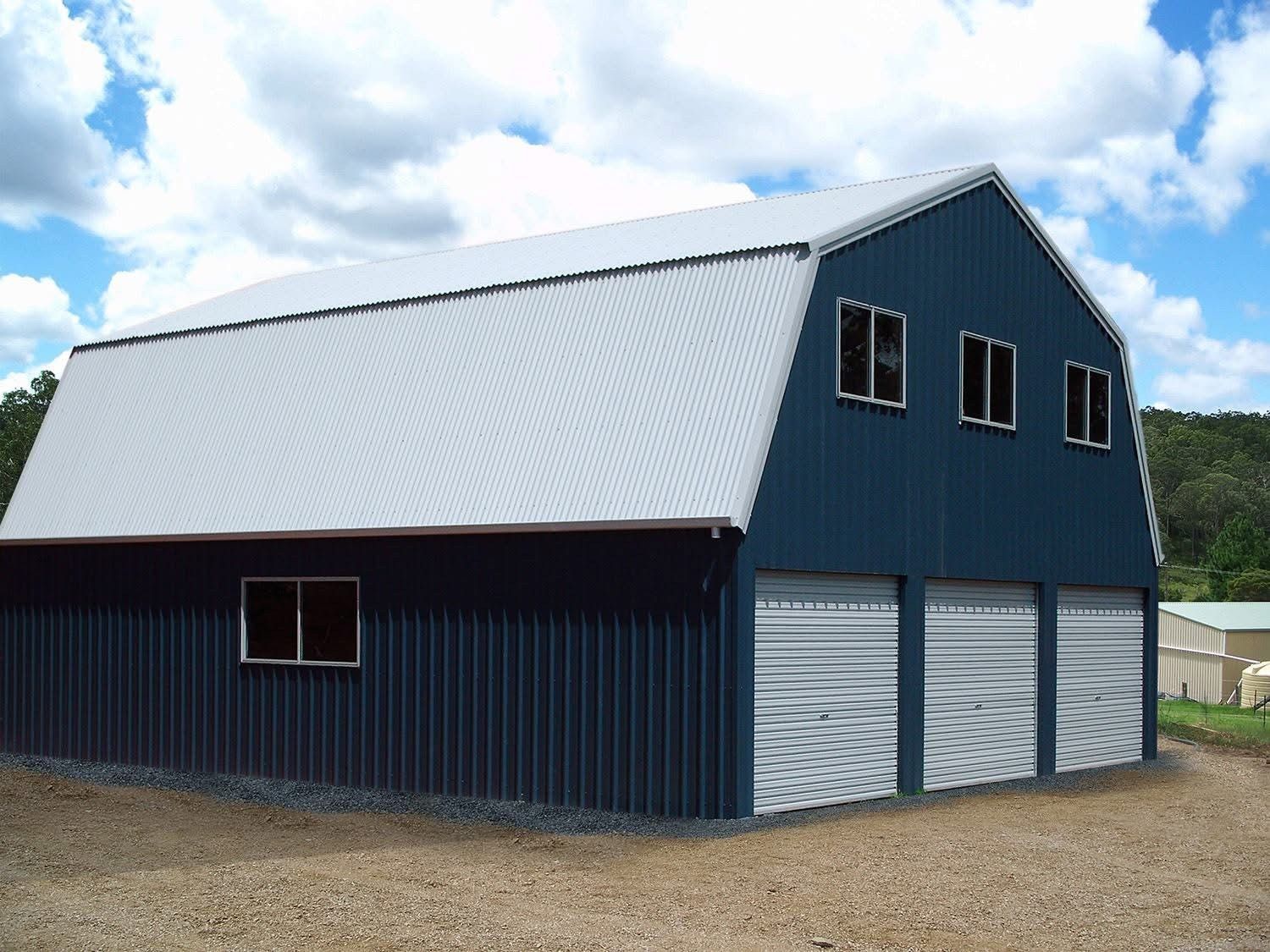 Blue barn with gray roof and three garage doors. Three windows are on the upper level.